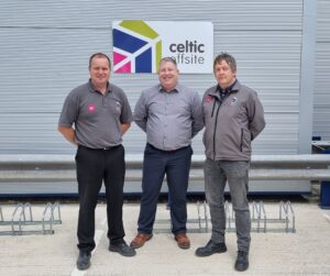 Three men stood facing the camera, wearing grey shirts and fleeces in front of a grey metal panel wall