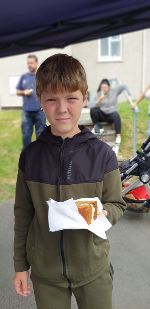 A young boy at a picnic holding a slice of Victoria sponge cake in a napkin.