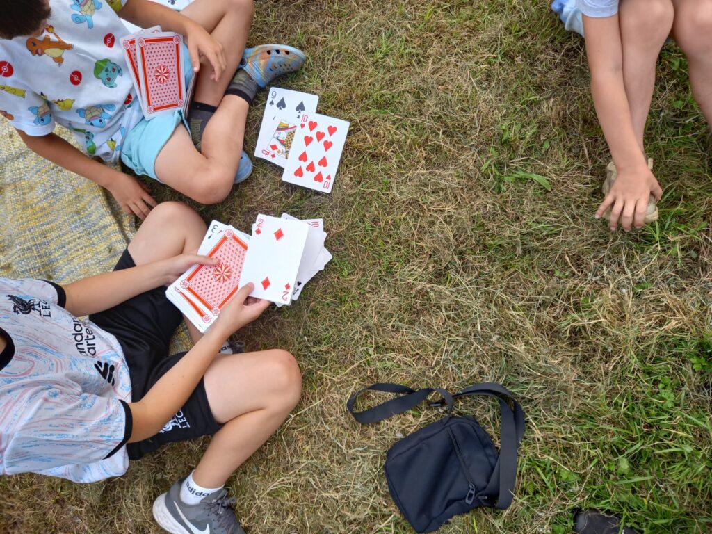 Children's hands holding playing cards as they sit on grass.