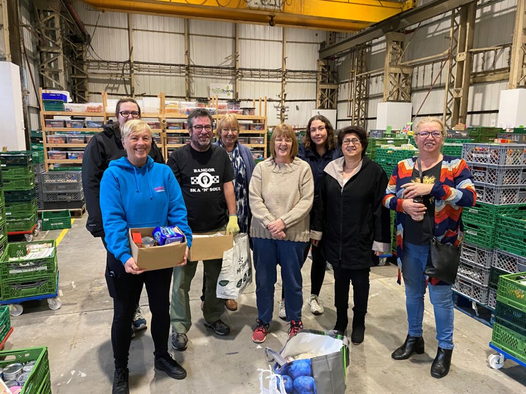 An image of United Welsh's floating support team at Cardiff Foodbank holding food parcels and smiling at the camera on their volunteering day