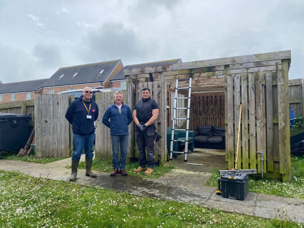 A photo of three people standing in front of a garden pergola.