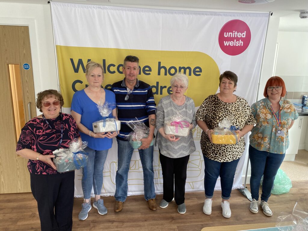 An image of people holding a hamper stood against a banner