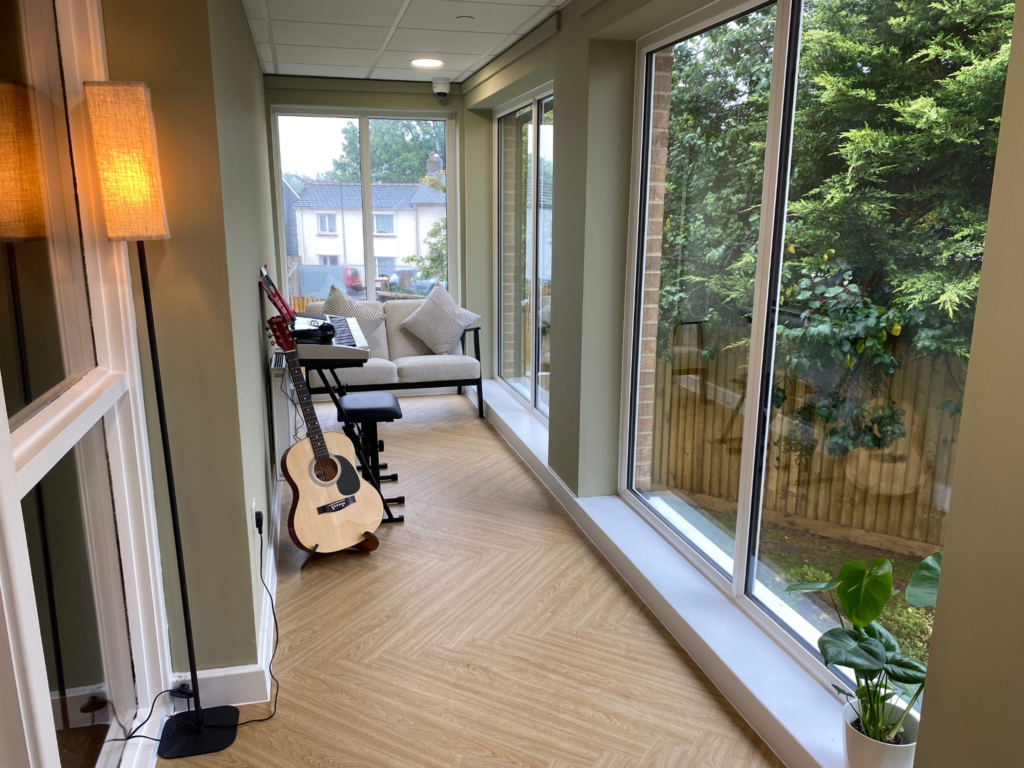 The hallway area of Acer House in Brynmawr. The right wall is full length windows, with wood flooring and musical instruments in the hallway.