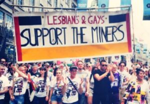 Members of LGSM marching with 'Lesbians & Gays Support the Miners' flag