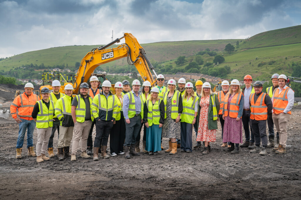 A group shot of stakeholders and partners on the site of the former Windsor Colliery. Everyone is wearing high vis jackets and hard hats, with a digger in the background.