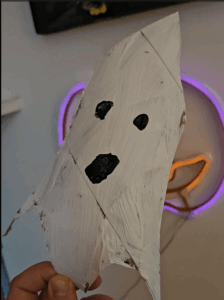 Hand holding a cardboard ghost painted white.