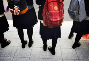 Photo of four children wearing school uniform and backpacks with their backs to the camera.