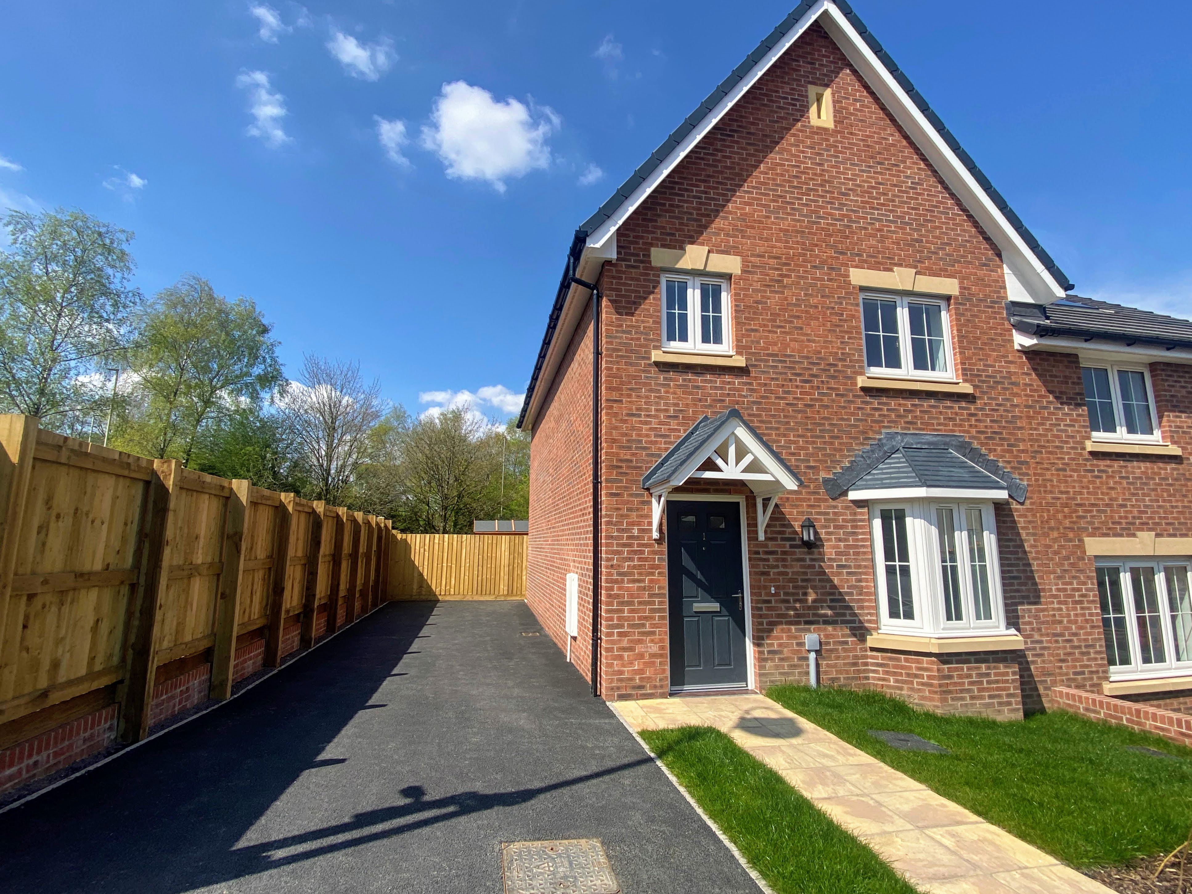 an image of a red brick house with white PVC bay window downstairs, grey door, grass front garden with beige paved path