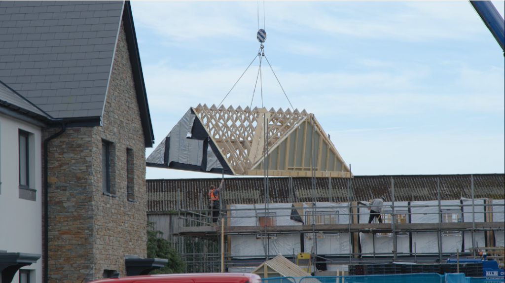 A photo of a roof of a timber frame home being placed on top of a new home.
