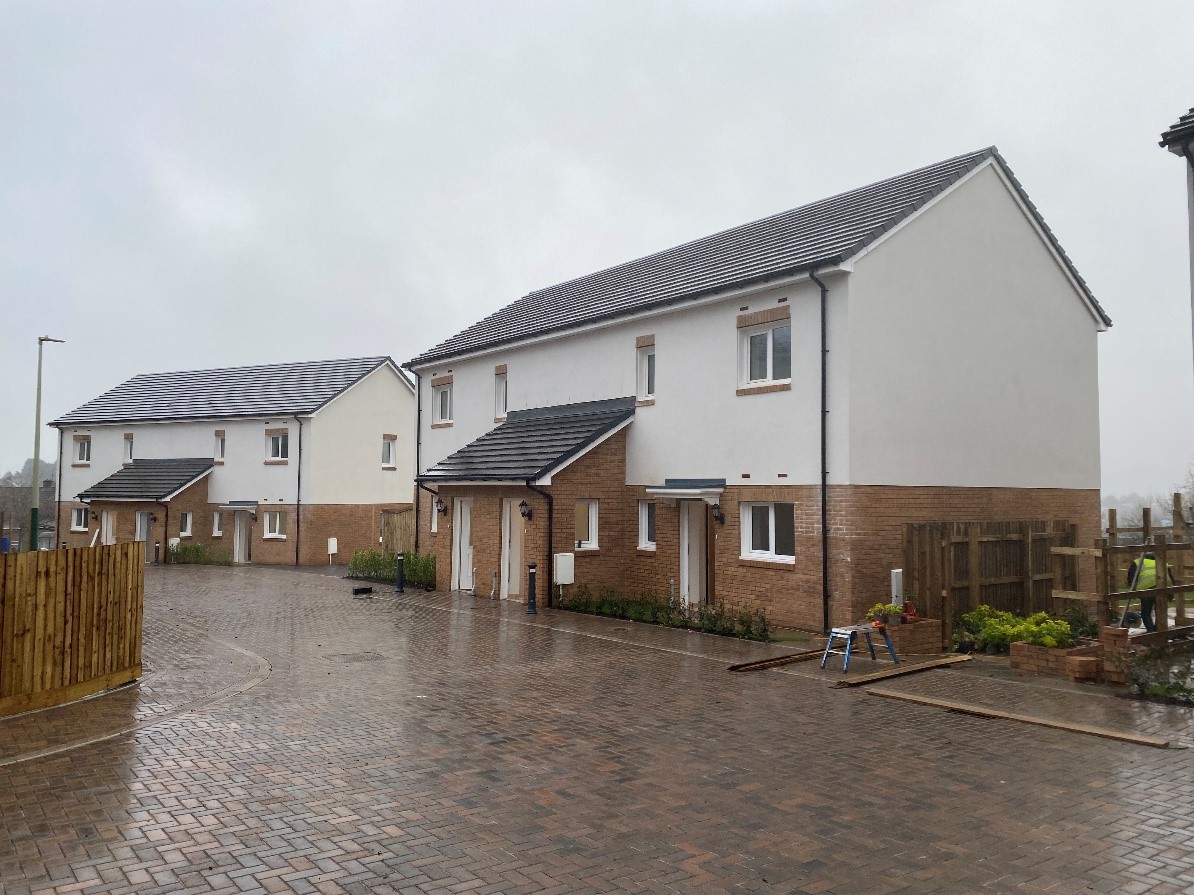 Row of three homes with grey slate rooves, white upper exterior walls and beige brick lower exterior walls and pink and grey paved driveways