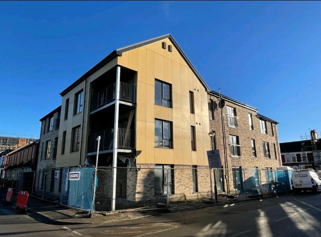 three story beige brick building showing two outdoor balconies on the first and second floor and glass windows in front of a blue sky