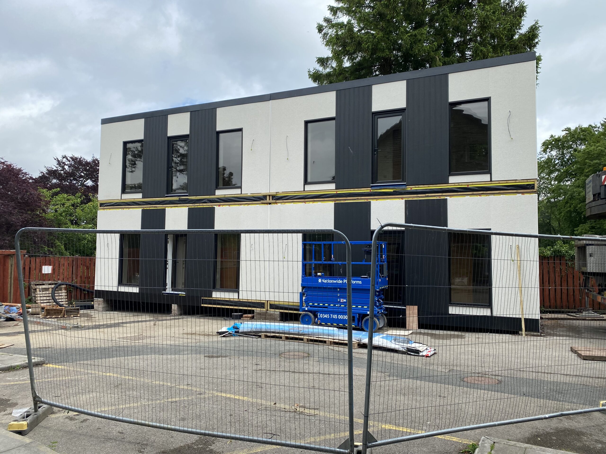 Two semi detached modular build apartments with white walls, large glass windows and black panels with grey metal fencing in front