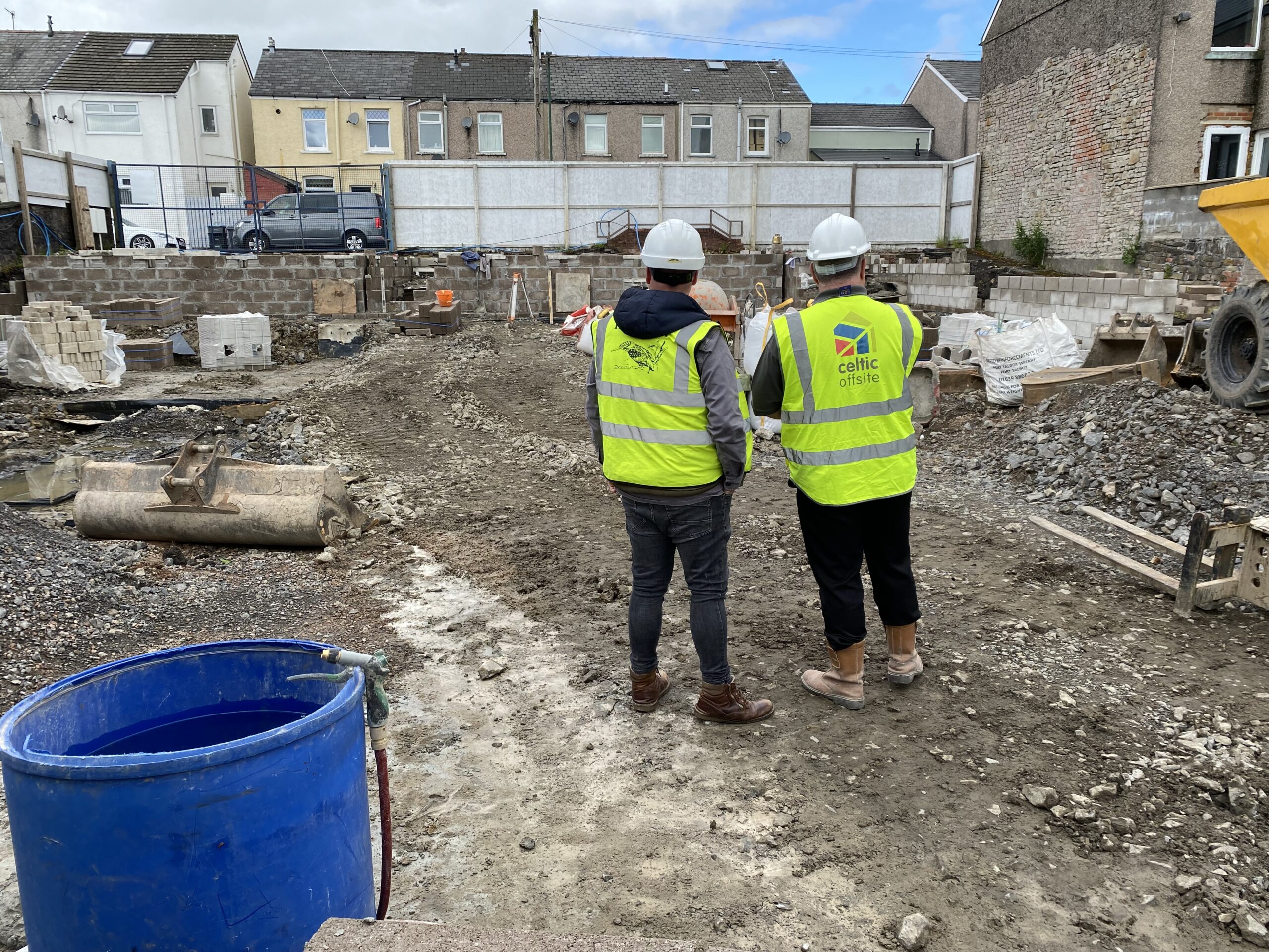 Two men looking onto a building site wearing yellow safety jackets and white hard hats