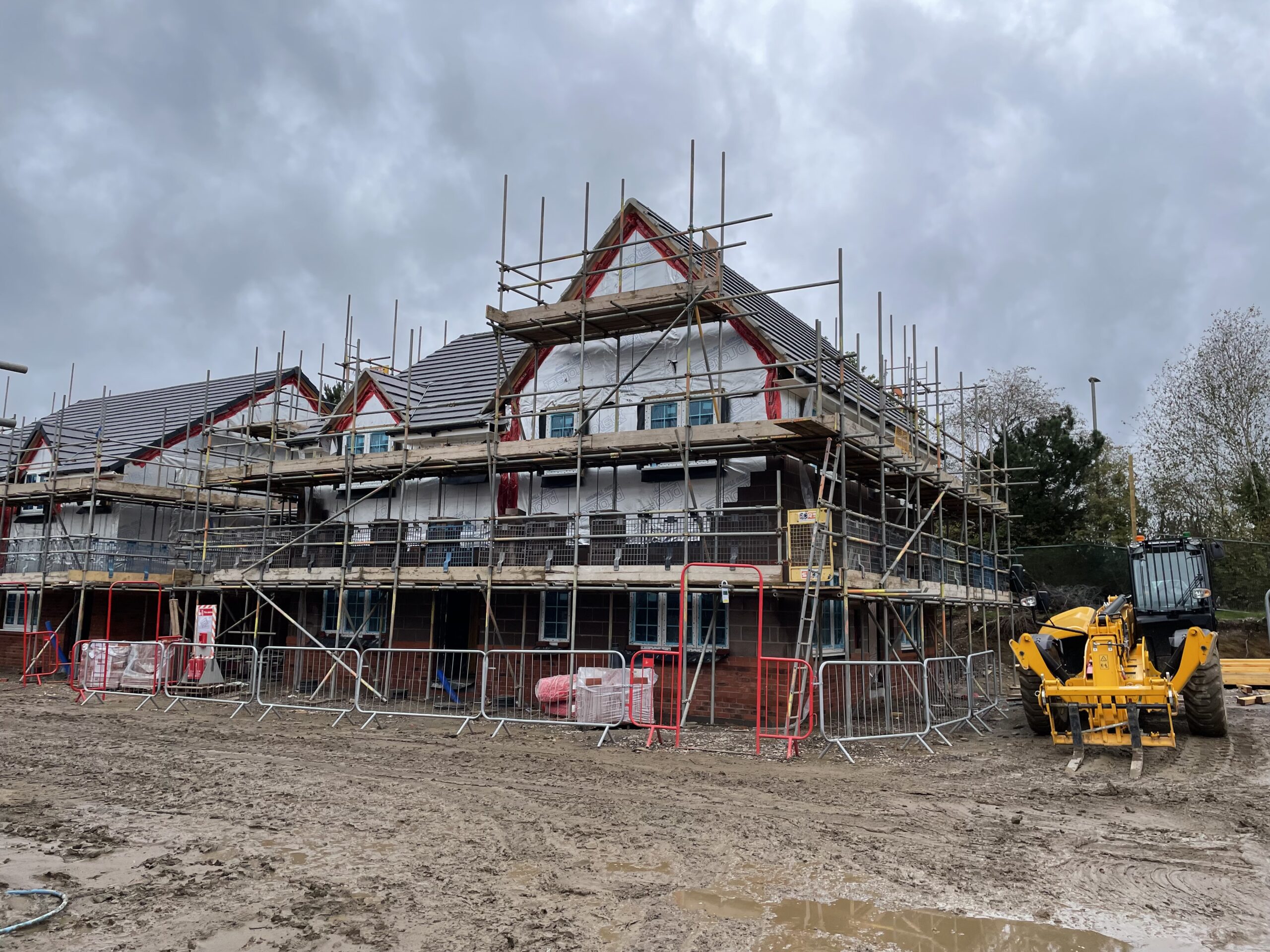 An image of a semi deatched house with white render and a pitch roof surrounded by scaffolding on a building site