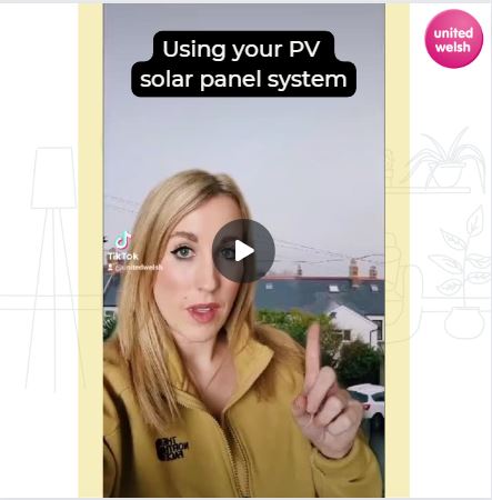 An image of a woman wearing a yellow jumper with the round magenta United Welsh logo. She is about to explain you must keep your PV solar panel system switched on and times to use appliances.