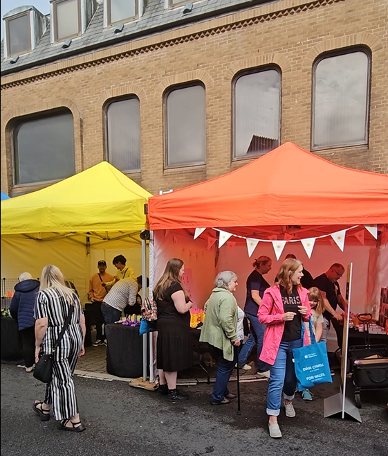 Photo of staff speaking to visitors to the Caerphilly Cheese under an orange gazebo.