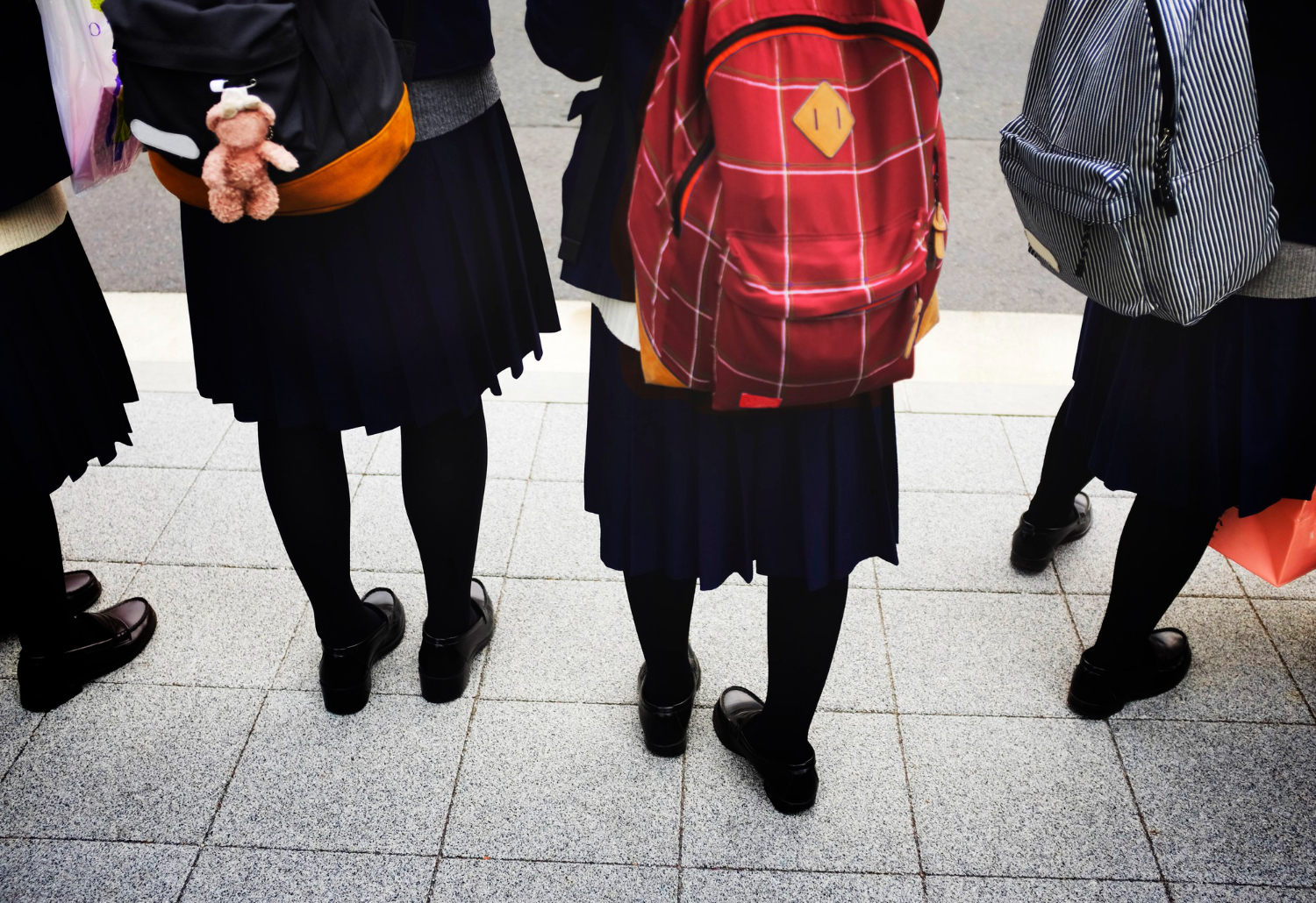 Photo of four children wearing school uniform and backpacks with their backs to the camera.